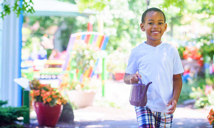 Young boy with watering can in Story Garden smiling